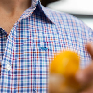 Person wearing a blue and red checkered shirt with a brand logo, holding a blurred object.