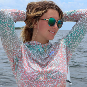 Woman wearing a patterned long-sleeve shirt and sunglasses on a boat with water and sky in the background