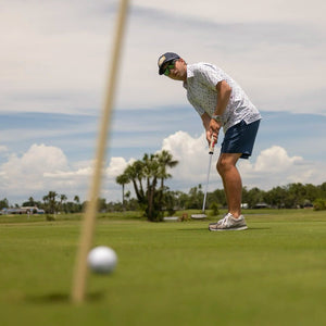 Man playing golf on a green course with trees and clouds in the background