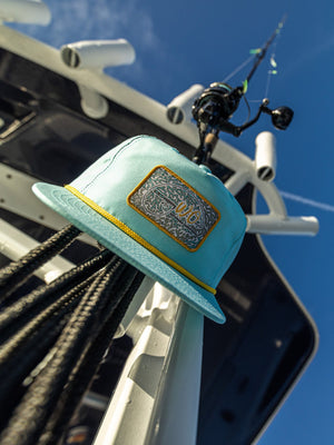 Teal fishing hat with logo attached to a boat against a blue sky
