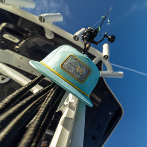 Teal fishing hat with logo attached to a boat against a blue sky