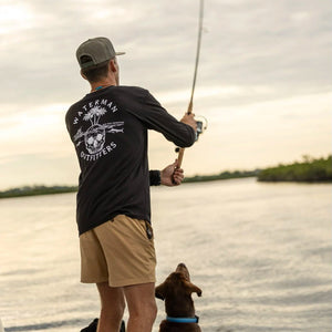 Man fishing on a boat with a dog by his side, wearing a black shirt with white text and graphics.