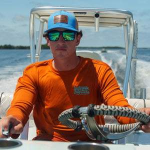 Man on a boat wearing an orange shirt and blue cap, holding a fishing rod.