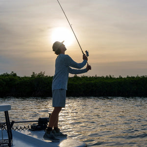 Person fishing on a boat at sunset with a serene water and forest background
