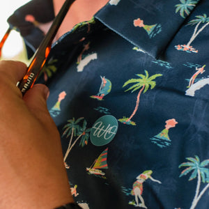 Person wearing a navy blue shirt with tropical pattern, holding sunglasses.