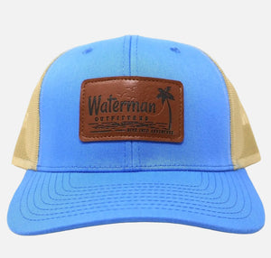 Blue and beige cap with a leather patch featuring 'Waterman Outfitters' on a white background