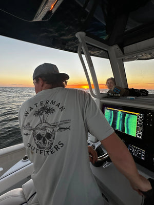 Person on a boat at sunset with 'Waterman Outfitters' shirt