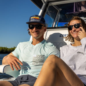 Two people sitting on a boat, smiling and wearing sunglasses.