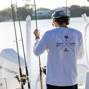 Man on a boat wearing a white long-sleeve shirt with a logo, holding fishing rods.