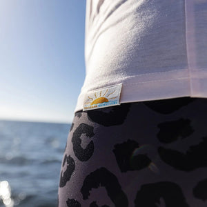 Person wearing a pink tank top with a logo and leopard print shorts by the ocean.