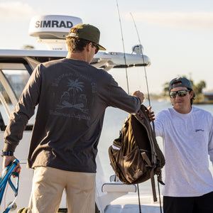 Two men on a boat with one holding a bag, wearing a Simrad branded hat.